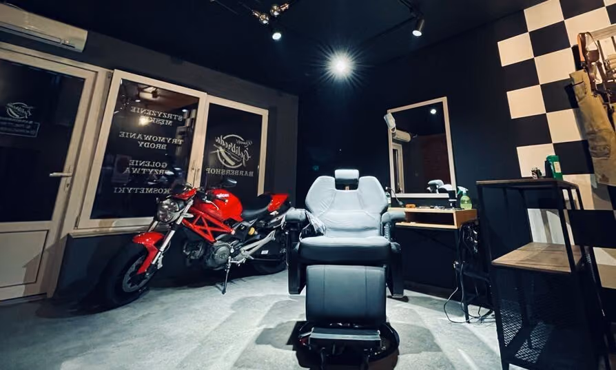Wnętrze barber shopu Konecki Golibroda w Końskich: fotel barberski, ściana w szachownicę i czerwony motocykl